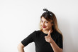 © shurkin_son - Indoor shot of attractive young woman in black dress and headwear having cheerful sly look, pointing her index finger at camera as if choosing you. Human facial expressions and emotions. Body language
