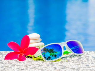 Wall Mural - Sunglasses with red frangipani (plumeria) flowers and stack of stone at the side of swimming pool. Vacation, beach, summer travel concept