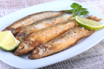 Deep frying small fish capelin and sliced lemon on white plate. Good snack to beer.