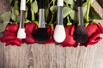 Poster - Conceptual image of make-up brushes next to roses on wooden background