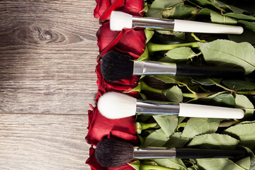 Poster - Conceptual image of make-up brushes next to roses on wooden background