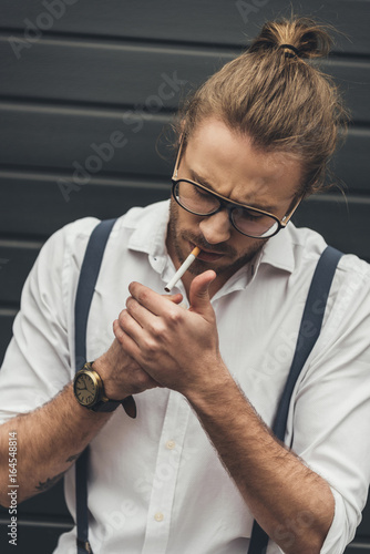 Fotografie, Obraz Close-up handsome stylish man in eyeglasses lighting cigarette with lighter