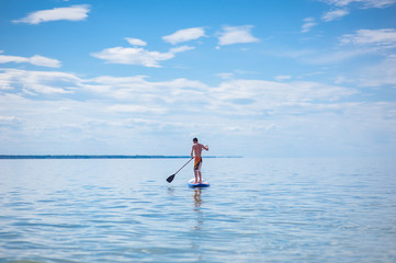 A young guy is floating on a sup board against the blue sky