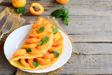 Wall Mural - Fruit omelet. Veggie stuffed omelet with fresh apricots on a white plate and an old wooden background with copy space for text. Healthy egg breakfast recipe