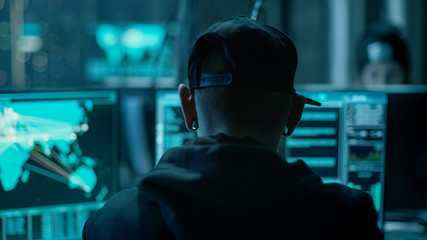 Aufkleber - Close-up Frame from the Back of Working Hacker Organizing Advanced Virus Attack on Corporate Servers. Place is Dark and Has Multiple displays.