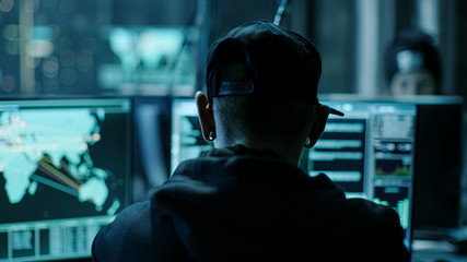Aufkleber - Close-up Frame from the Back of Working Hacker Organizing Advanced Virus Attack on Corporate Servers. Place is Dark and Has Multiple displays.