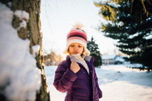 Young Girl Looking At Thumb By Tree In Snowy Landscape 
