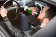 A young handsome bearded man with a bottle of beer or a low-alcohol drink at the wheel of a car. Driving in a state of intoxication