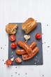 Grilled Sausages on a black stone plate on white wooden table with tomatoes, garlic, salt and pepper