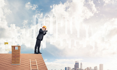 Engineer man standing on roof and looking in binoculars. Mixed m