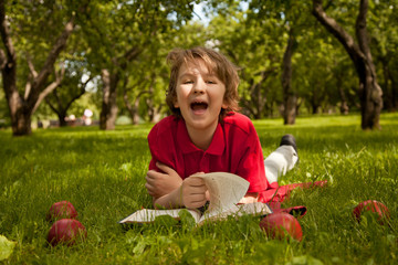 teen boy reading a book in the green summer apple trees park