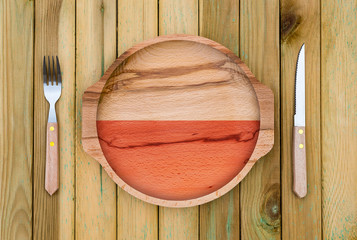 Wall Mural - Concept of Polish cuisine. Wooden plate with a Poland flag, fork and knife on a wooden background