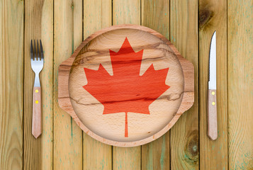 Wall Mural - Concept of Canadian cuisine. Wooden plate with a Canada flag, fork and knife on a wooden background