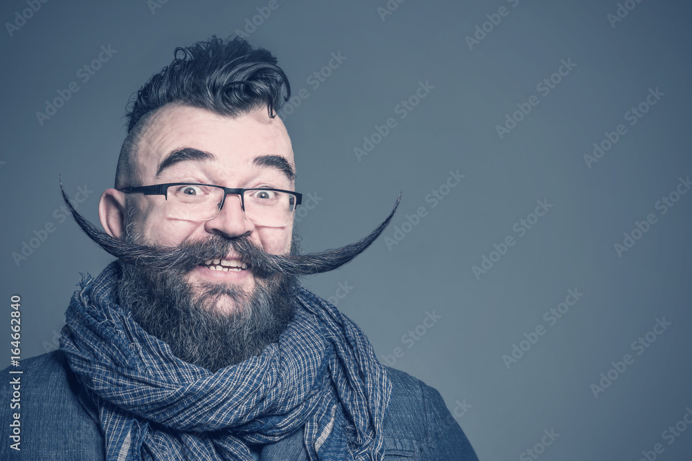 Smiling bearded man with a mohawk hairstyle and a very long mustache on a gray background - obrazy, fototapety, plakaty 