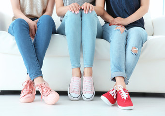 Wall Mural - Young women with beautiful legs in jeans and sneakers sitting on sofa