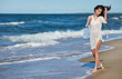 © ZoomTeam - Young woman walking in water wearing white beach  dress