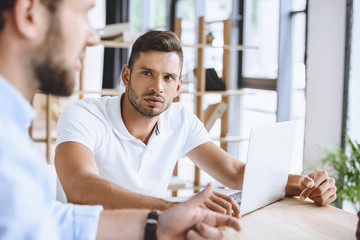 Canvas Print - portrait of young businessman with laptop on meeting with coworkers in office