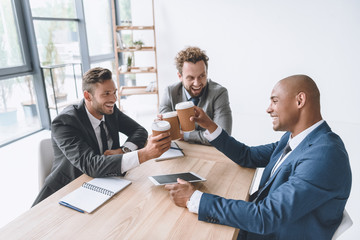 Canvas Print - multicultural group of smiling businessmen clinking disposable cups of coffee at meeting