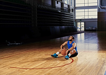 Wall Mural - Black professional basketball player sits on a floor in a game hall.