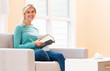 © Tierney - Happy young woman reading a book on her couch at home