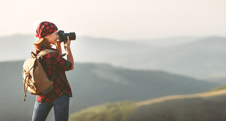 Woman tourist photographer with camera on top of mountain at sunset  a hike in summer