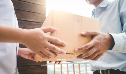 Close up hand of asia woman are receive a box from delivery man with sun light in delivery service concept.