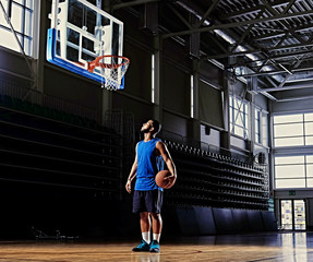 Wall Mural - Basketball player holds a ball over the hoop in a game hall.