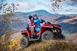 © anatoliy_gleb - Happy women in jackets and hats on red quad bike at the hill makes selfie on the phone with mountains in blurred background. Sunny autumn day