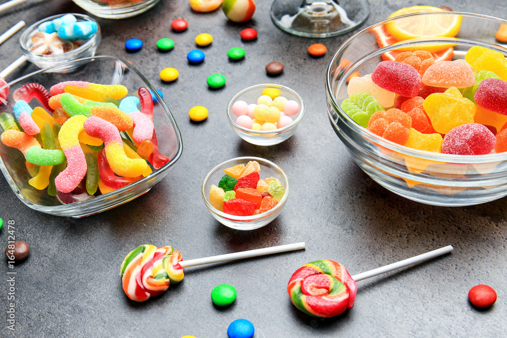 Bowls with delicious candies on grey background