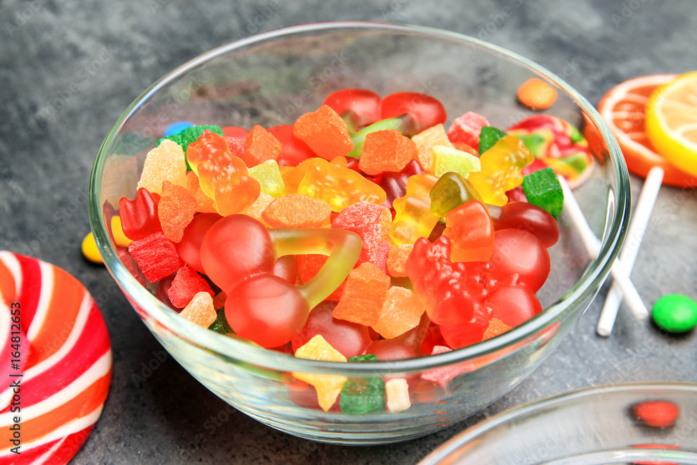 Bowl with delicious candies on grey background