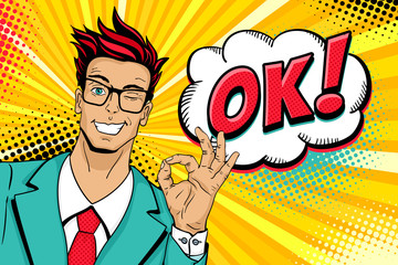 Wall Mural - Wow pop art male face. Young handsome man in glasses smiles, winks and shows okay sign and OK! speech bubble. Vector illustration in retro comic style. Vector pop art background. Invitation poster.