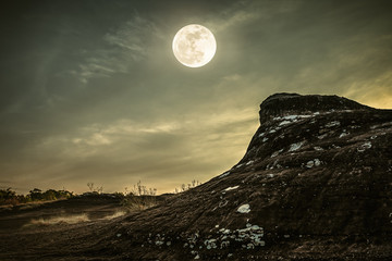 Landscape of rock against sky and full moon above wilderness area in forest.