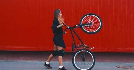 Wall Mural - Young stylish Caucasian female riding her bicycle, urban background. 4K UHD RAW edited footage