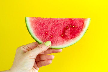 Beautiful feminine hands holding fresh tasty red appetizing watermelon on bright yellow background. Summer Concept.