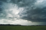 Fototapeta Morze - Storm cloud over green fields forests and hills