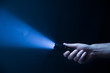The flashlight in the man's hand from the right side of the frame in black and blue color isolated on black background