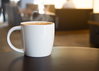 A cup of coffee latte with smoke on the cup on the table in coffee shop.