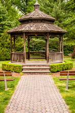 Front Of Gazebo With Wood And Steel Benches In Front. Outdoor Gazebo With Shrubs And Grass. Shady Retreat In Backyard. Outdoor Rotunda Summerhouse. Outside Platform.