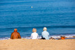 © GoodPics - family sitting on beach towels in the sand. Three persons, one man and two women.