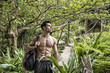 © theartofphoto - Young muscular topless man with backpack and phone looking away on background of tropical forest.