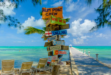 Colorful Signpost By The Caribbean Sea And A Jetty At Rum Point, Grand Cayman, Cayman Islands