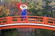 © Gavin Hellier Photography/Stocksy - Asia, Japan, Honshu, Kansai Region, Kyoto, Geisha holding an ornate red paper umbrella standing on a traditional style Japanese red bridge