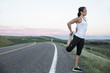 © Robinson Media Inc/Stocksy - a young athletic woman stretching on the side of a paved road