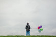 © Cindy Prins/Stocksy - Boy standing in a field against a cloudy sky holding balloons