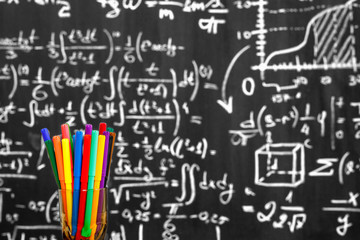 Back to school background with colorful felt pens and blurred math formulas written by white chalk on the black school chalkboard