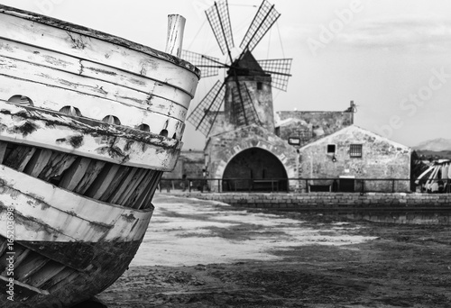Fotografie, Obraz Dettagli barca in primo piano con mulino a vento sullo sfondo nella salina di Tr