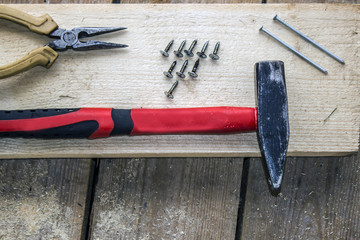 pliers, screws, hammer, nails - on a bar and wooden unplaned boards. Hand tools for building a frame house.