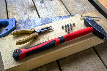 hacksaw, pliers, screws, hammer, nails - on a bar and wooden unplaned boards. Hand tools for building a frame house.