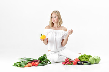 Sticker - Beautiful blond woman in white clothes and lots of fresh vegetables on white background. Girl holds bell pepper