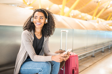 happy young black woman listening music with headphones and mobile phone at the airport